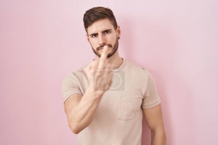 Foto de Hispanic man with beard standing over pink background showing middle finger, impolite and rude fuck off expression - Imagen libre de derechos