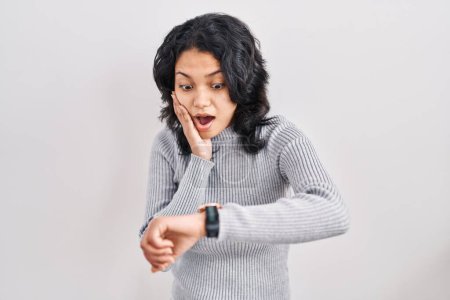 Photo for Hispanic woman with dark hair standing over isolated background looking at the watch time worried, afraid of getting late - Royalty Free Image