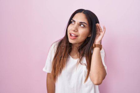Téléchargez les photos : Jeune femme arabe debout sur fond rose souriant avec la main sur l'oreille en écoutant une rumeur ou des commérages. concept de surdité. - en image libre de droit