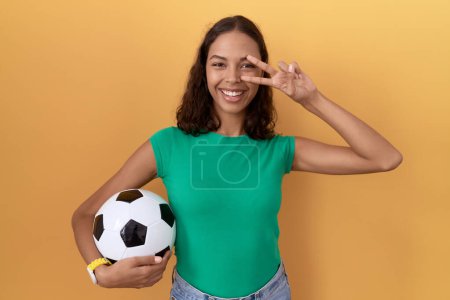 Téléchargez les photos : Jeune femme hispanique tenant le ballon faisant symbole de paix avec les doigts sur le visage, souriant gai montrant la victoire - en image libre de droit