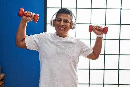 Photo for Young latin man listening to music using dumbbells training at sport center - Royalty Free Image