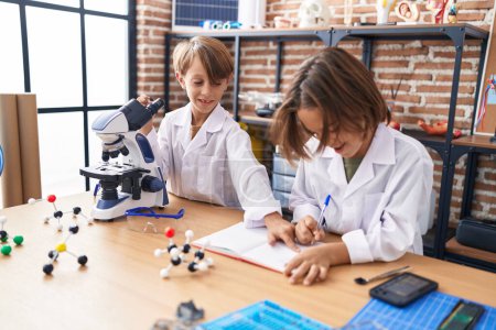 Photo for Adorable boys students using microscope writing notes at laboratory classroom - Royalty Free Image