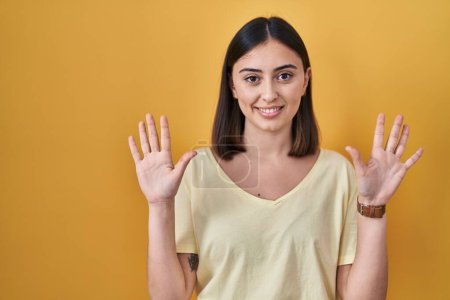 Photo for Hispanic girl wearing casual t shirt over yellow background showing and pointing up with fingers number ten while smiling confident and happy. - Royalty Free Image