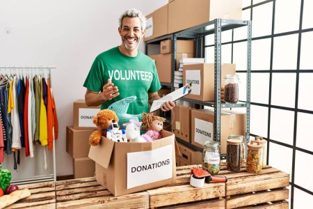 Téléchargez les photos : Middle age grey-haired man volunteer reading document holding toys at charity center - en image libre de droit