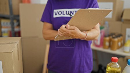 Photo for Middle age hispanic woman volunteer writing on document checking products at charity center - Royalty Free Image