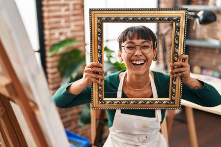 Photo for Young beautiful woman sitting at art studio with empty frame smiling and laughing hard out loud because funny crazy joke. - Royalty Free Image