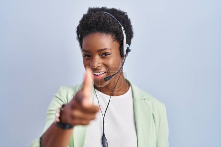 Foto de Mujer afroamericana con auriculares de agente de call center apuntando con los dedos a la cámara con cara alegre y divertida. buena energía y vibraciones. - Imagen libre de derechos
