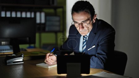 Téléchargez les photos : Homme d'âge moyen travailleur d'affaires en utilisant touchpad prendre des notes au bureau - en image libre de droit