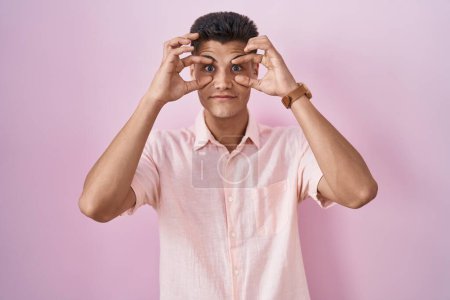 Téléchargez les photos : Jeune homme hispanique debout sur fond rose essayant d'ouvrir les yeux avec les doigts, somnolent et fatigué pour la fatigue matinale - en image libre de droit