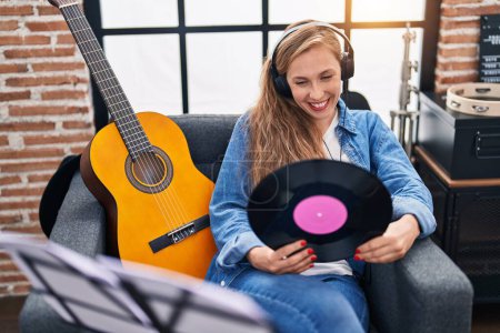 Téléchargez les photos : Jeune femme blonde musicienne écoutant de la musique tenant un disque vinyle au studio de musique - en image libre de droit