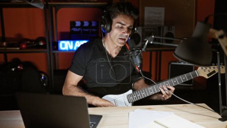 Foto de Joven músico hispano cantando canción tocando guitarra eléctrica en estudio de radio - Imagen libre de derechos