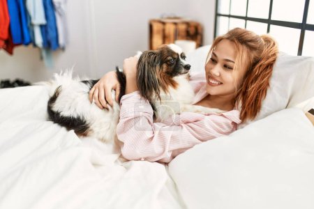 Téléchargez les photos : Jeune femme caucasienne couchée sur le lit étreignant chien dans la chambre - en image libre de droit