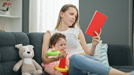 Photo for Mother and daughter reading book while playing with hoops at home - Royalty Free Image