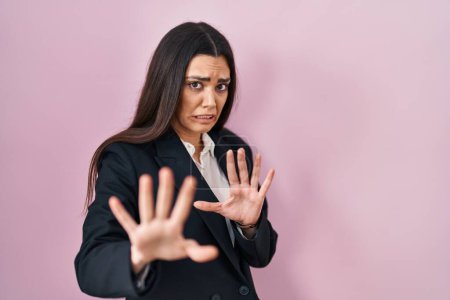 Photo for Young brunette woman wearing business style over pink background afraid and terrified with fear expression stop gesture with hands, shouting in shock. panic concept. - Royalty Free Image