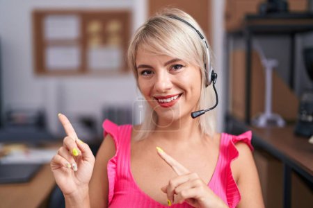 Photo for Young caucasian woman wearing call center agent headset smiling and looking at the camera pointing with two hands and fingers to the side. - Royalty Free Image