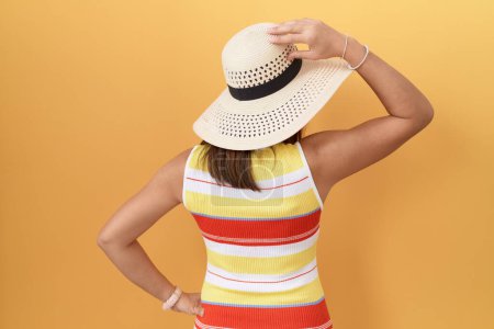 Foto de Mujer china de mediana edad con sombrero de verano sobre fondo amarillo hacia atrás pensando en la duda con la mano en la cabeza - Imagen libre de derechos