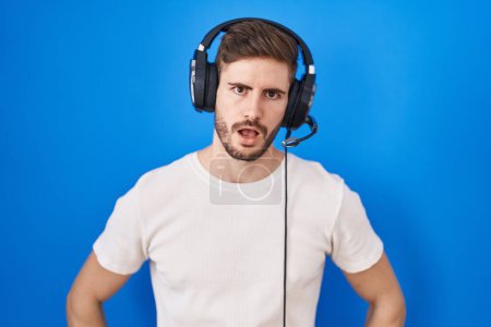 Photo for Hispanic man with beard listening to music wearing headphones in shock face, looking skeptical and sarcastic, surprised with open mouth - Royalty Free Image