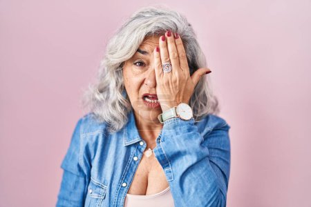 Foto de Mujer de mediana edad con el pelo gris de pie sobre fondo rosa bostezando cansado cubriendo media cara, ojo y boca con la mano. cara duele en el dolor. - Imagen libre de derechos