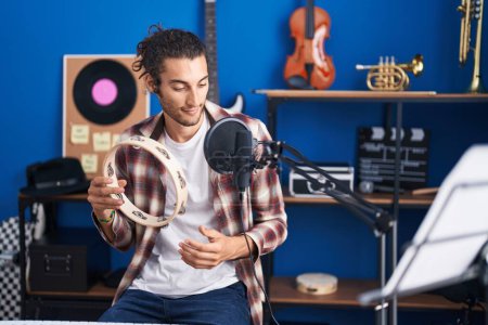 Téléchargez les photos : Young hispanic man musician singing song playing tambourine at music studio - en image libre de droit