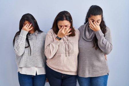 Photo for Mother and two daughters standing over blue background tired rubbing nose and eyes feeling fatigue and headache. stress and frustration concept. - Royalty Free Image