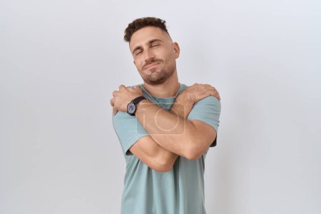 Téléchargez les photos : Hispanic man with beard standing over white background hugging oneself happy and positive, smiling confident. self love and self care - en image libre de droit