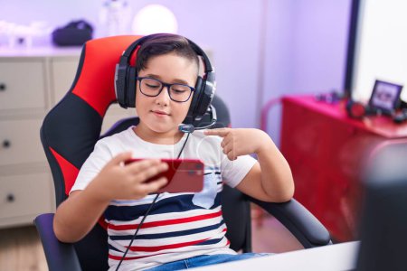 Téléchargez les photos : Jeune enfant hispanique jouant à des jeux vidéo avec smartphone souriant heureux pointant avec la main et le doigt - en image libre de droit