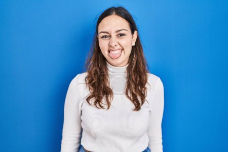 Photo for Young hispanic woman standing over blue background sticking tongue out happy with funny expression. emotion concept. - Royalty Free Image