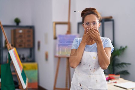 Téléchargez les photos : Brunette femme peinture au studio d'art choqué couvrant la bouche avec les mains pour erreur. concept secret. - en image libre de droit