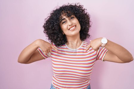 Foto de Joven mujer de Oriente Medio de pie sobre fondo rosa mirando confiado con sonrisa en la cara, señalándose con los dedos orgullosos y felices. - Imagen libre de derechos