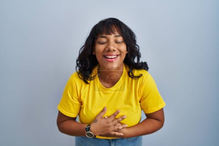 Téléchargez les photos : Femme hispanique debout sur fond bleu souriant et riant fort à haute voix parce que drôle blague folle avec les mains sur le corps. - en image libre de droit