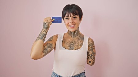 Foto de Mujer hispana con brazo amputado sonriendo confiada sosteniendo tarjeta de crédito sobre fondo rosa aislado - Imagen libre de derechos