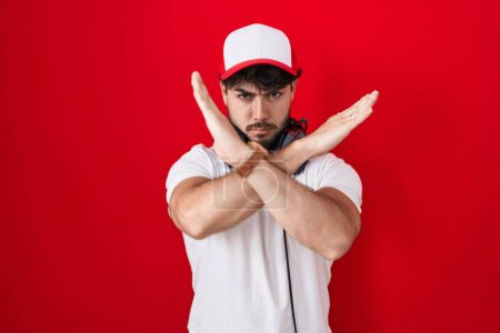 Foto de Hombre hispano con barba usando sombrero de gamer y auriculares expresión de rechazo cruzando brazos haciendo signo negativo, cara enojada - Imagen libre de derechos