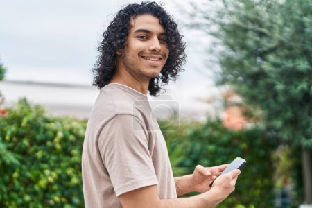 Photo for Young latin man smiling confident using smartphone at park - Royalty Free Image