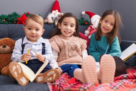 Photo for Group of kids drawing on notebook sitting on sofa by christmas decoration at home - Royalty Free Image