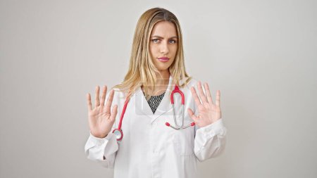 Téléchargez les photos : Jeune femme blonde médecin debout avec une expression sérieuse faisant geste d'arrêt sur fond blanc isolé - en image libre de droit
