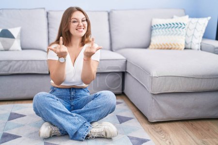 Foto de Young caucasian woman sitting on the floor at the living room showing middle finger doing fuck you bad expression, provocation and rude attitude. screaming excited - Imagen libre de derechos