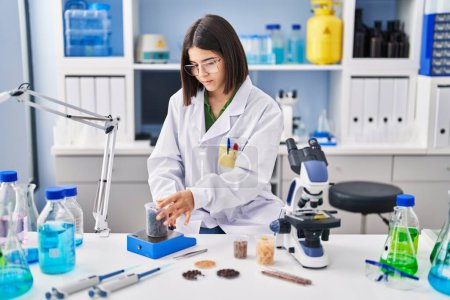 Photo for Young beautiful hispanic woman scientist weighing sample at laboratory - Royalty Free Image