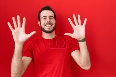 Photo for Young hispanic man wearing casual red t shirt showing and pointing up with fingers number ten while smiling confident and happy. - Royalty Free Image
