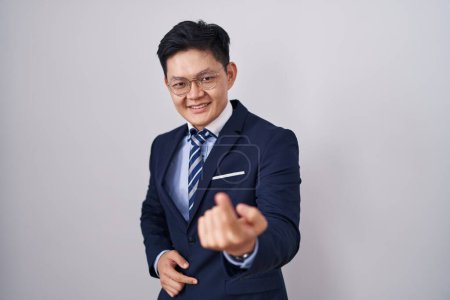Foto de Joven asiático hombre vistiendo negocio traje y corbata señas venir aquí gesto con mano invitando a bienvenida feliz y sonriente - Imagen libre de derechos