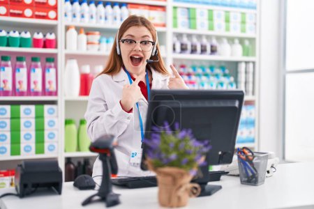 Téléchargez les photos : Femme rousse travaillant à la pharmacie pharmacie portant casque souriant heureux pointant avec la main et le doigt - en image libre de droit