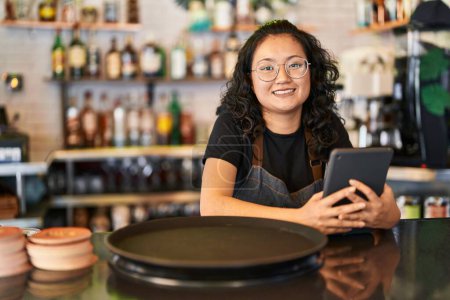 Téléchargez les photos : Young chinese woman waitress smiling confident using touchpad at restaurant - en image libre de droit