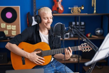 Foto de Young caucasian man musician singing song playing classical guitar at music studio - Imagen libre de derechos