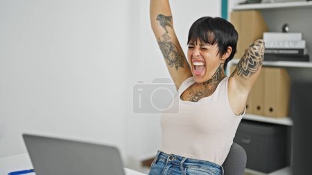 Foto de Mujer hispana con amputado brazo trabajador de negocios utilizando portátil trabajando con gesto ganador en la oficina - Imagen libre de derechos