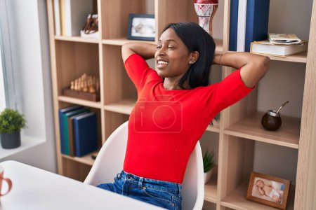 Photo for Young african american woman relaxed with hands on head sitting on table at home - Royalty Free Image