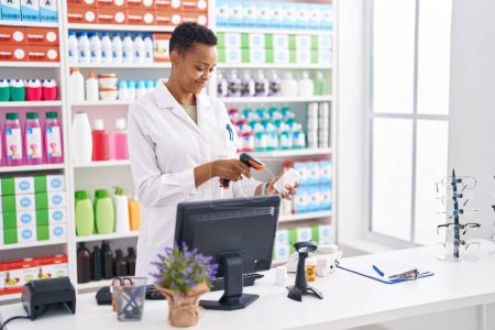Téléchargez les photos : Afro-américaine femme pharmacien numérisation pilules bouteille à la pharmacie - en image libre de droit