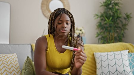 Photo for African american woman holding pregnancy test with serious face at home - Royalty Free Image