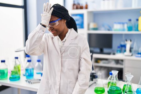 Téléchargez les photos : Femme afro-américaine travaillant au laboratoire scientifique surpris avec la main sur la tête pour erreur, rappelez-vous erreur. oublié, mauvais concept de mémoire. - en image libre de droit