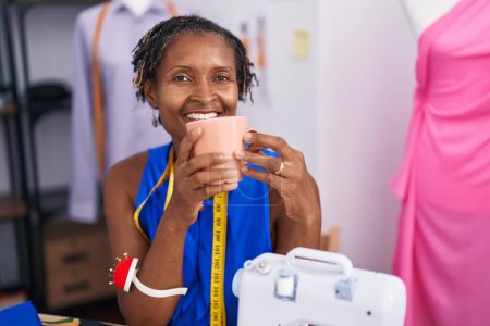 Foto de Middle age african american woman tailor smiling confident drinking coffee at atelier - Imagen libre de derechos