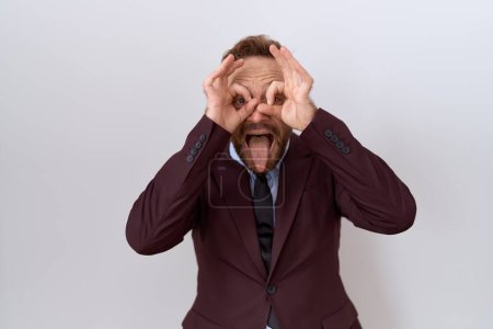 Photo for Middle age business man with beard wearing suit and tie doing ok gesture like binoculars sticking tongue out, eyes looking through fingers. crazy expression. - Royalty Free Image