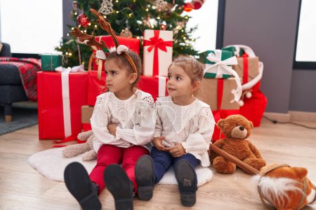Photo for Two kids sitting on floor by christmas tree with unhappy expression at home - Royalty Free Image
